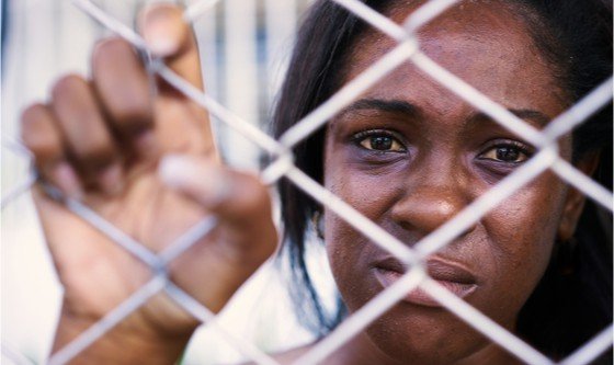 Woman behind a wire fence, looking upset 