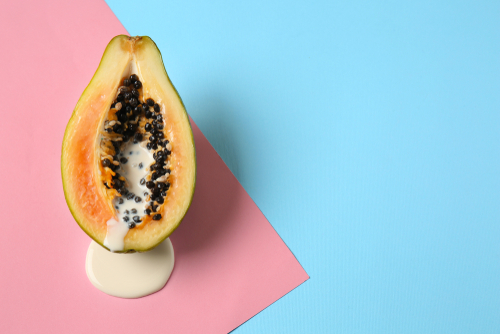 Half of papaya with dripping white liquid on color background