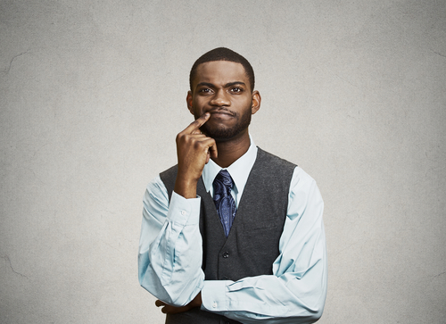 young, puzzled business man thinking, deciding deeply something, finger on lips looking confused, unsure isolated grey wall background with texture. Emotion facial expression feeling