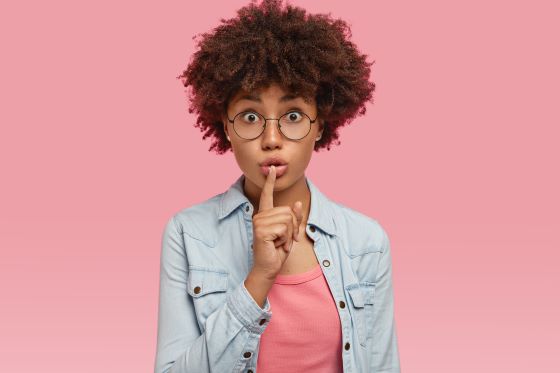 young woman putting her finger over lips to signify keeping quiet