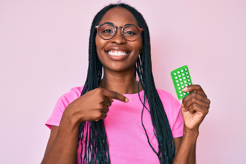 African american woman with braids holding birth control pills pointing finger to one