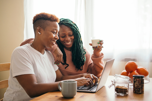 Happy gay couple having breakfast working on laptop